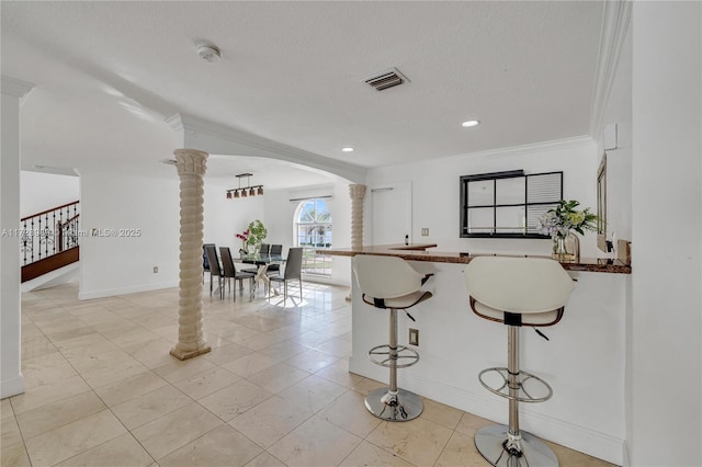 kitchen with crown molding, decorative columns, a textured ceiling, and a breakfast bar area