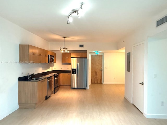 kitchen with dark countertops, a sink, brown cabinetry, appliances with stainless steel finishes, and visible vents