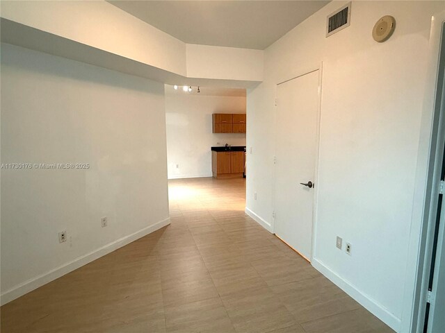 hall featuring visible vents, baseboards, and light floors