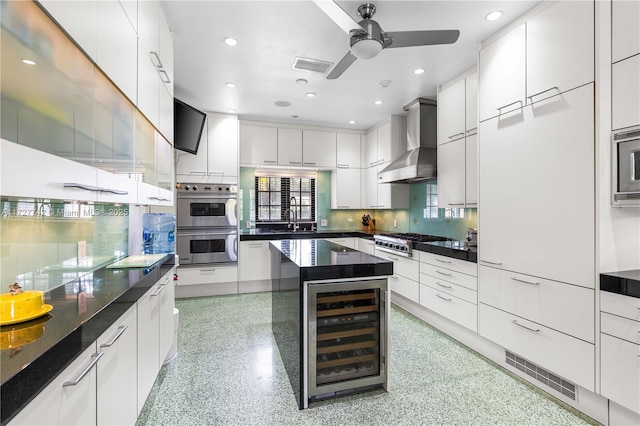 kitchen with wine cooler, appliances with stainless steel finishes, sink, white cabinets, and wall chimney range hood