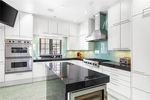 kitchen with appliances with stainless steel finishes, decorative backsplash, white cabinets, sink, and wall chimney exhaust hood