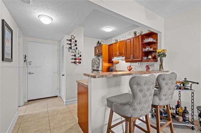 kitchen featuring fridge, light tile patterned floors, kitchen peninsula, and a breakfast bar area