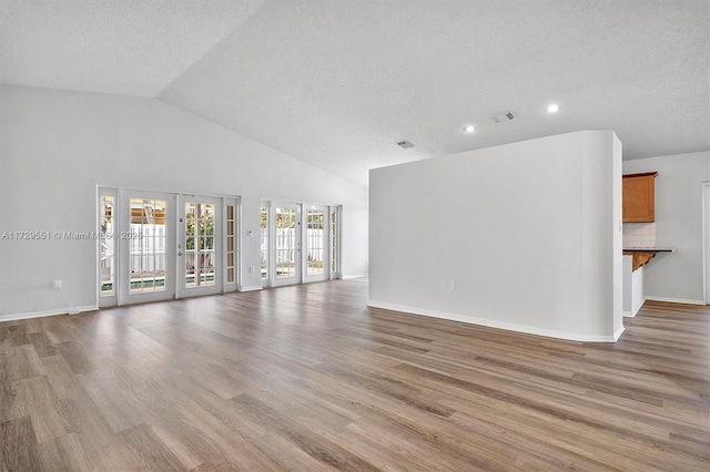 unfurnished living room with high vaulted ceiling, a textured ceiling, light hardwood / wood-style floors, and french doors