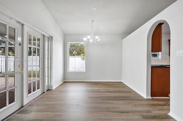 unfurnished dining area with lofted ceiling, a chandelier, hardwood / wood-style floors, and a textured ceiling