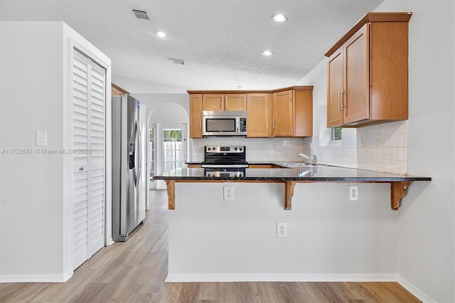 kitchen with light hardwood / wood-style floors, appliances with stainless steel finishes, a kitchen breakfast bar, and kitchen peninsula