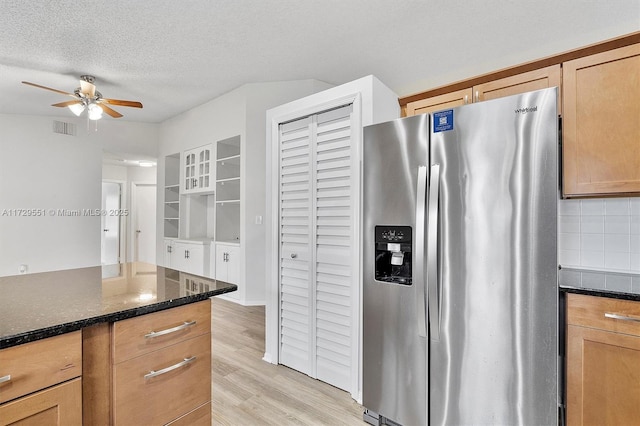 kitchen featuring backsplash, dark stone counters, light hardwood / wood-style floors, stainless steel refrigerator with ice dispenser, and a textured ceiling