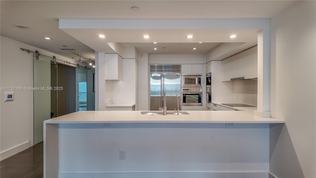 kitchen featuring white cabinets, kitchen peninsula, built in appliances, and a barn door