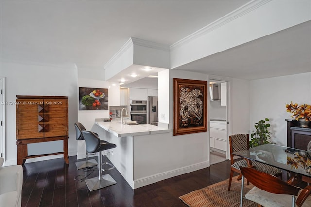 kitchen featuring white cabinetry, a breakfast bar area, kitchen peninsula, stainless steel appliances, and dark wood-type flooring