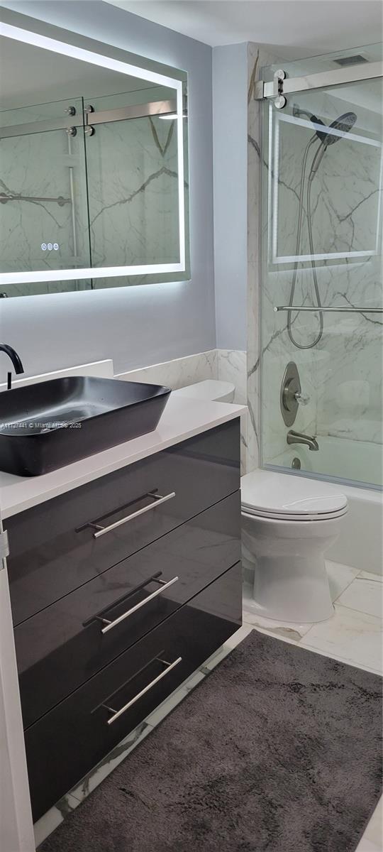 full bathroom featuring vanity, combined bath / shower with glass door, and toilet