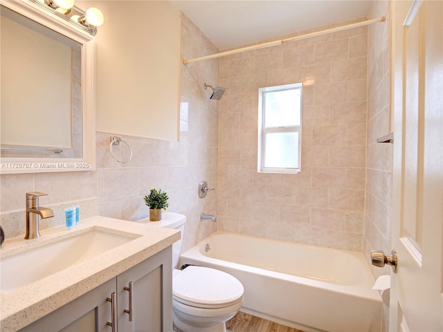 full bathroom with toilet, tiled shower / bath combo, tile walls, vanity, and backsplash