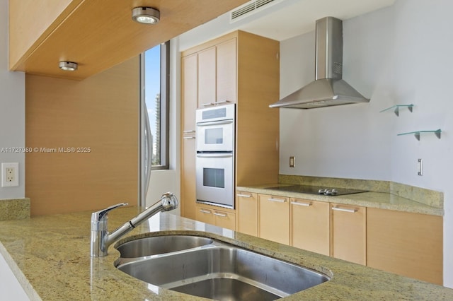 kitchen featuring sink, black electric stovetop, light stone counters, wall chimney range hood, and stainless steel double oven