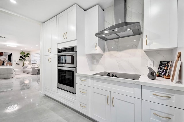 kitchen with tasteful backsplash, white cabinetry, stainless steel double oven, black electric stovetop, and wall chimney range hood