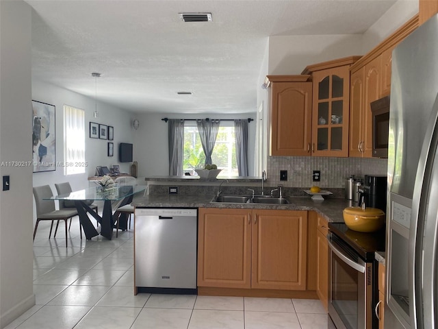 kitchen with light tile patterned floors, sink, dark stone countertops, kitchen peninsula, and stainless steel appliances