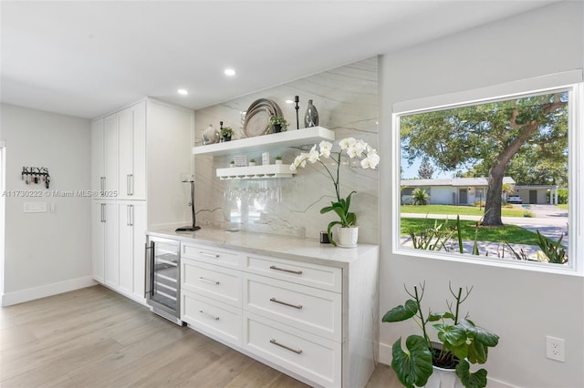 bar featuring wine cooler, white cabinetry, light stone countertops, and a healthy amount of sunlight