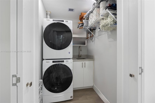 laundry room featuring stacked washer and dryer, sink, cabinets, and light hardwood / wood-style flooring