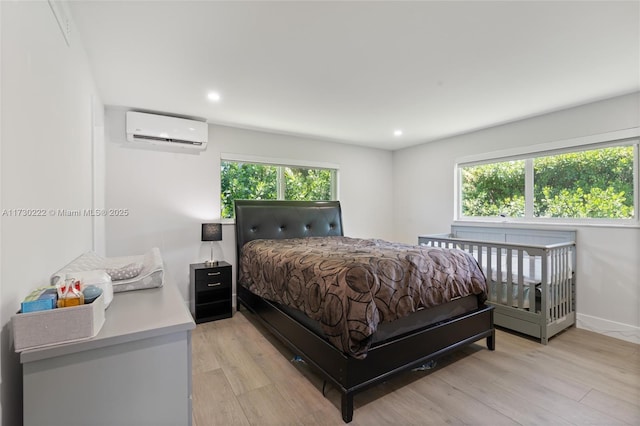 bedroom with multiple windows, a wall unit AC, and light wood-type flooring