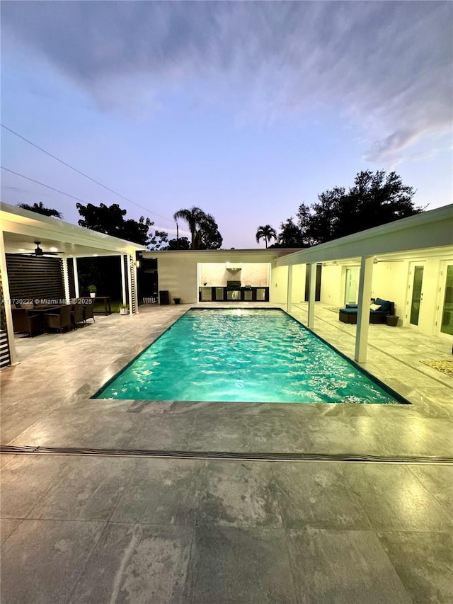 pool at dusk featuring ceiling fan, an outdoor living space, and a patio