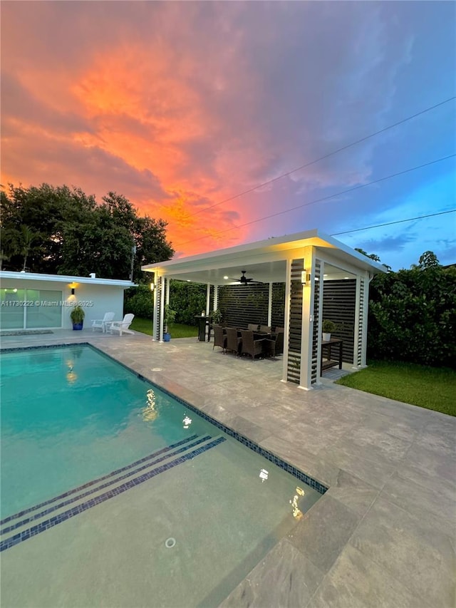 pool at dusk with an outbuilding, ceiling fan, an outdoor living space, and a patio