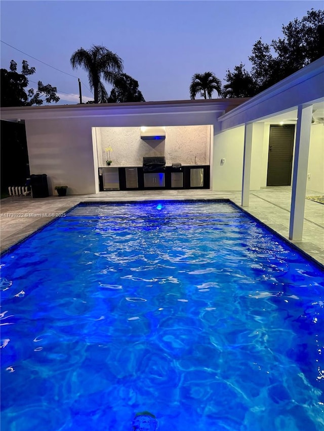 pool at dusk featuring a patio area and exterior kitchen