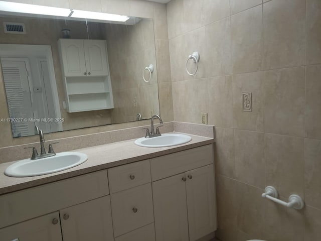 bathroom with tile walls, double vanity, visible vents, and a sink