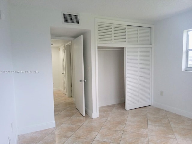 unfurnished bedroom featuring light tile patterned floors, visible vents, baseboards, and a closet