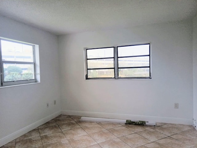 spare room with light tile patterned flooring, baseboards, and a textured ceiling