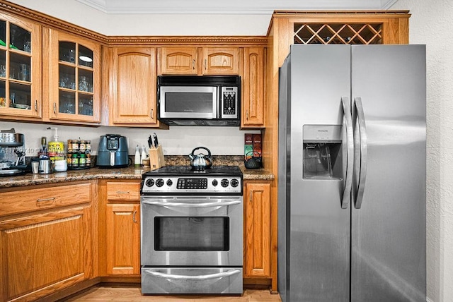 kitchen with ornamental molding, light wood-type flooring, dark stone counters, and appliances with stainless steel finishes