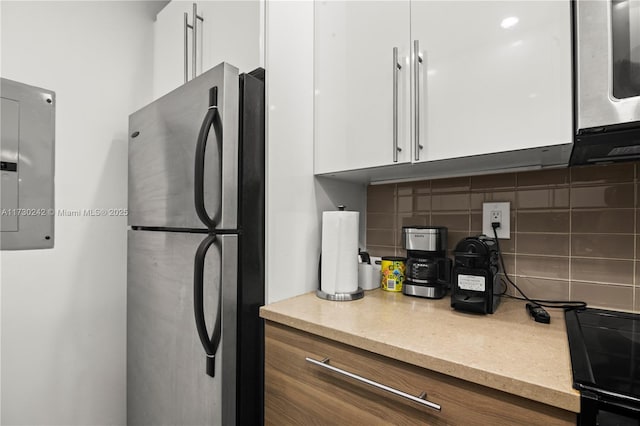 kitchen featuring backsplash, white cabinets, electric panel, and stainless steel fridge