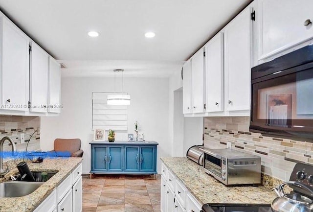 kitchen with light stone countertops, white cabinetry, sink, hanging light fixtures, and stove