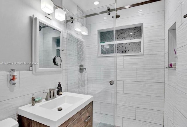 bathroom with a shower with door, tile walls, and vanity