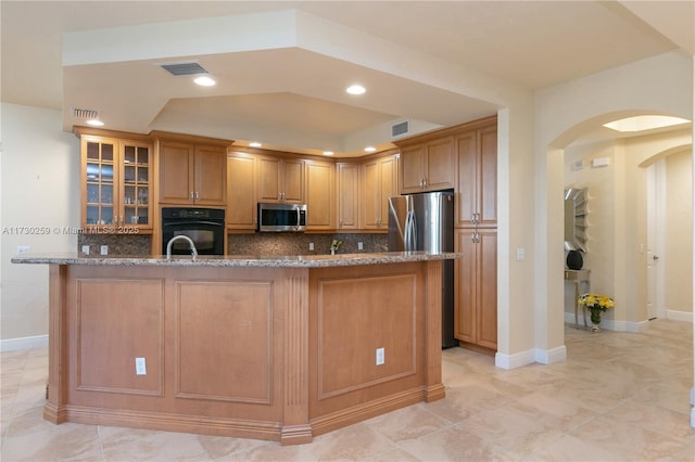 kitchen with appliances with stainless steel finishes, sink, backsplash, a kitchen island with sink, and stone counters