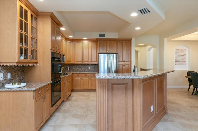 kitchen featuring light stone counters, backsplash, stainless steel fridge, and a center island with sink