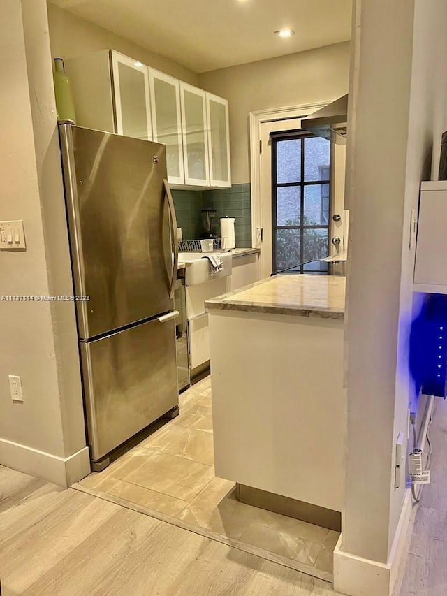 kitchen with backsplash, white cabinets, stainless steel fridge, and light stone counters