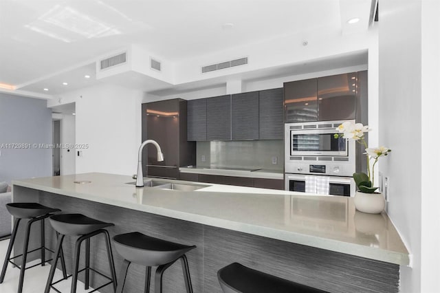 kitchen featuring stainless steel microwave, a kitchen bar, sink, kitchen peninsula, and white oven