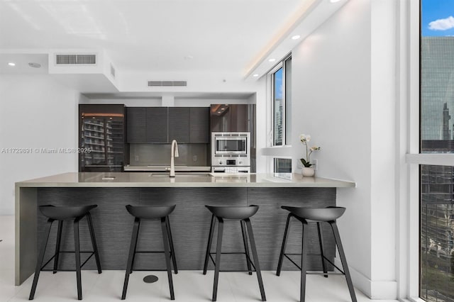 kitchen with decorative backsplash, sink, kitchen peninsula, a breakfast bar, and stainless steel microwave