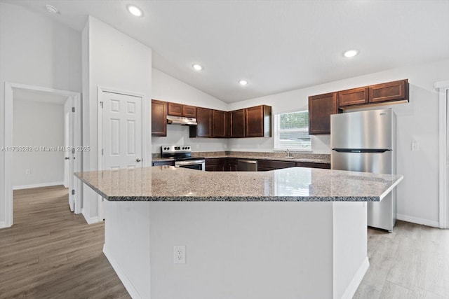 kitchen with appliances with stainless steel finishes, sink, a kitchen island, light stone counters, and lofted ceiling