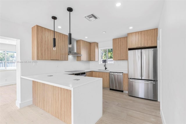 kitchen featuring wall chimney range hood, light hardwood / wood-style flooring, hanging light fixtures, stainless steel appliances, and kitchen peninsula