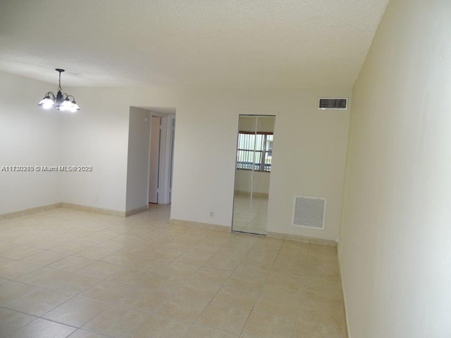 empty room with a textured ceiling, light tile patterned floors, and a chandelier