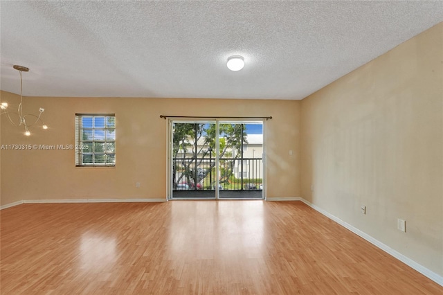 unfurnished room featuring a chandelier, light hardwood / wood-style flooring, and a textured ceiling