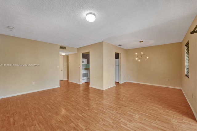 empty room featuring light hardwood / wood-style floors, a textured ceiling, and a notable chandelier