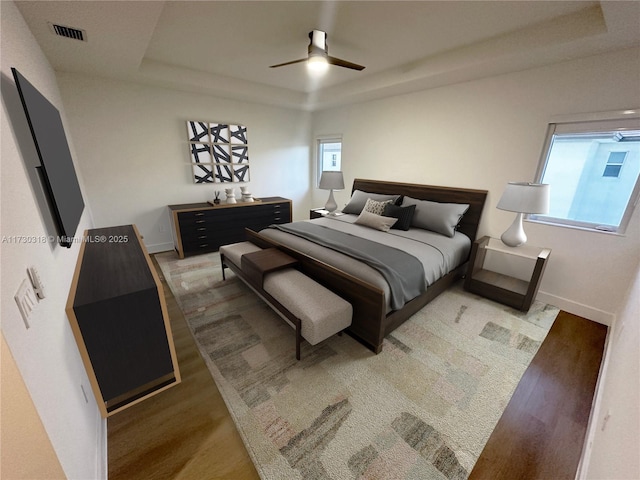 bedroom featuring ceiling fan, hardwood / wood-style flooring, multiple windows, and a tray ceiling