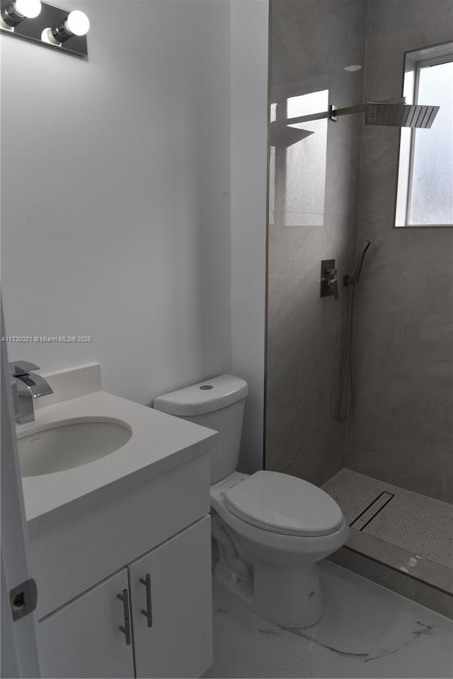 bathroom with tiled shower, vanity, and toilet