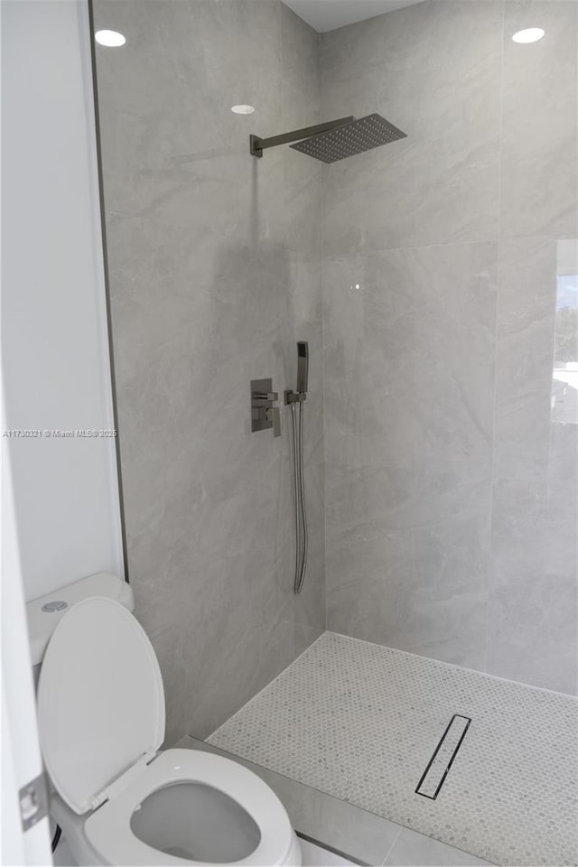 bathroom featuring tiled shower, toilet, and tile patterned flooring