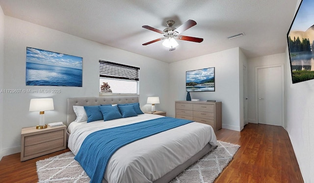 bedroom with ceiling fan, a textured ceiling, and dark hardwood / wood-style flooring