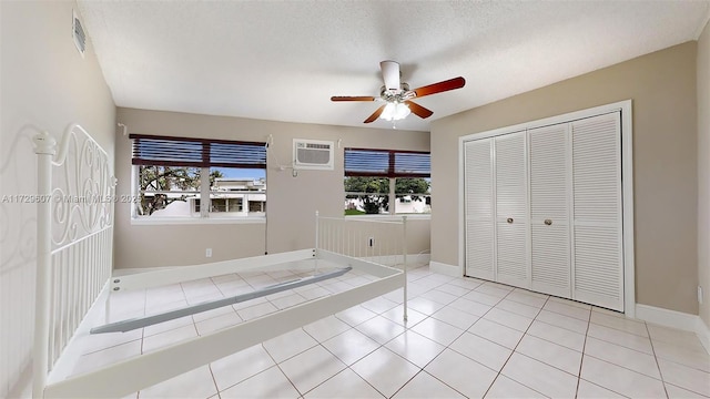 unfurnished bedroom with an AC wall unit, a textured ceiling, a closet, light tile patterned flooring, and ceiling fan