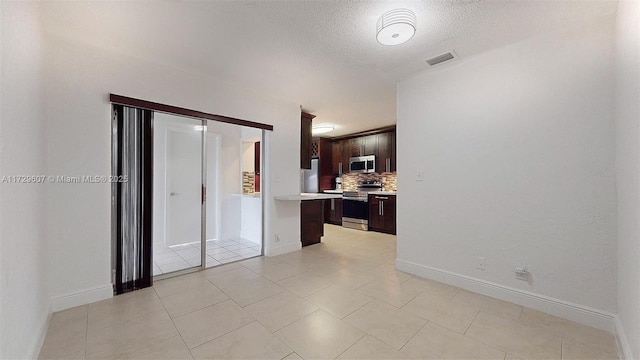 kitchen with dark brown cabinets, backsplash, a textured ceiling, and appliances with stainless steel finishes