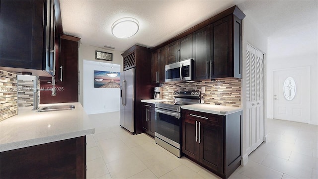 kitchen featuring a textured ceiling, dark brown cabinetry, stainless steel appliances, decorative backsplash, and sink