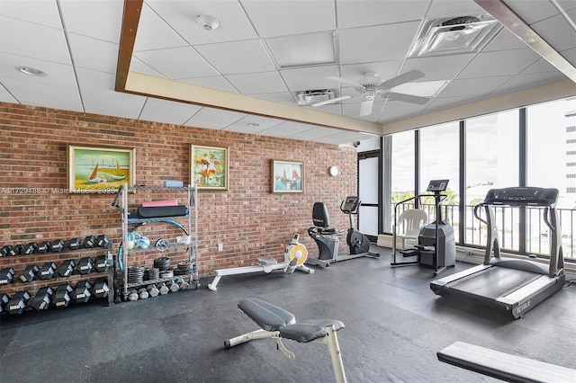 gym featuring ceiling fan, brick wall, and a drop ceiling