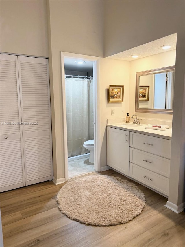 bathroom featuring hardwood / wood-style flooring, toilet, walk in shower, and vanity