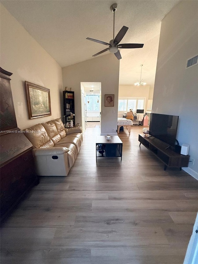 living room with light wood-type flooring, ceiling fan with notable chandelier, and high vaulted ceiling